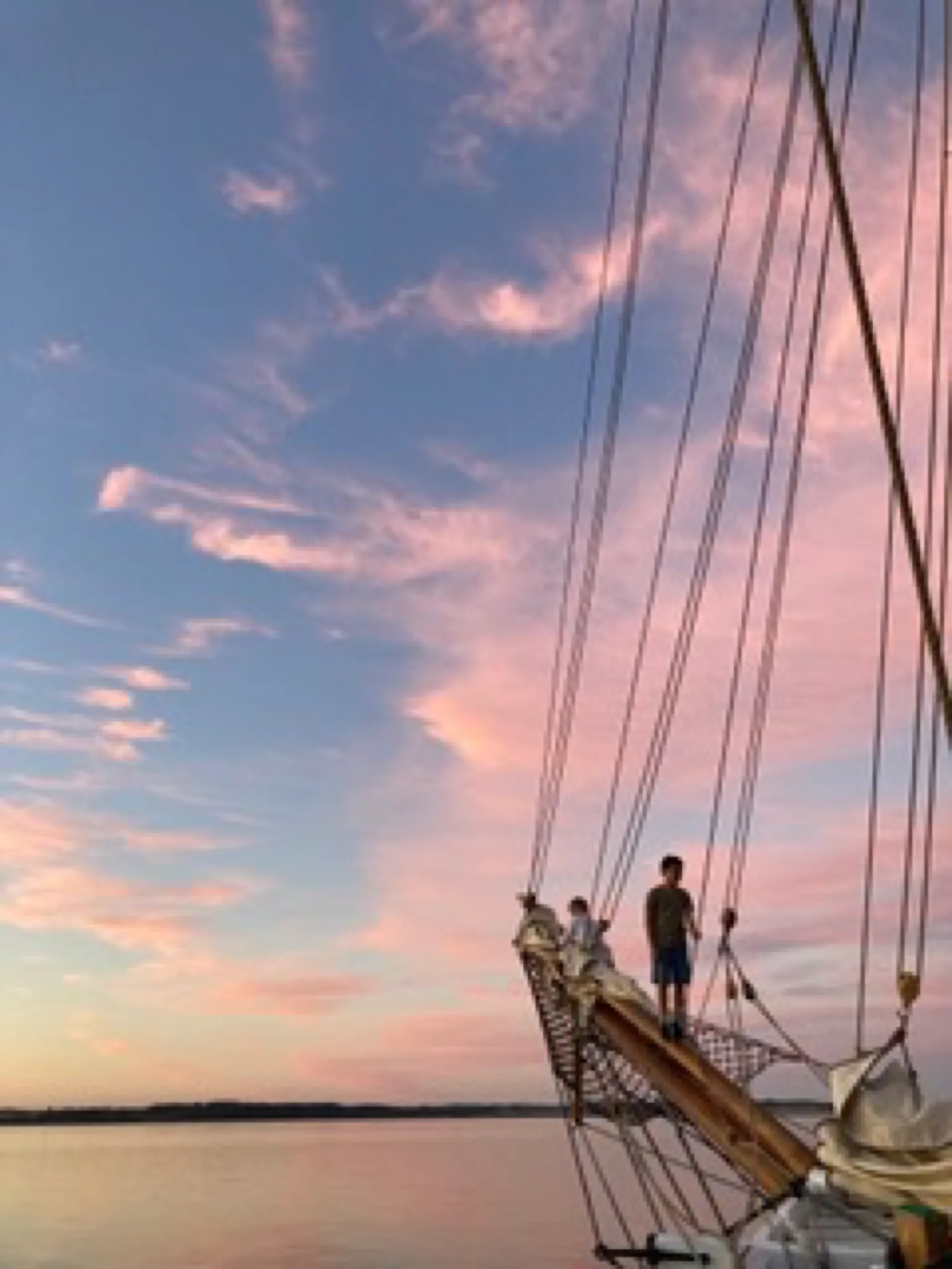 To børn står på bovsprydet under en lyserød aftenhimmel